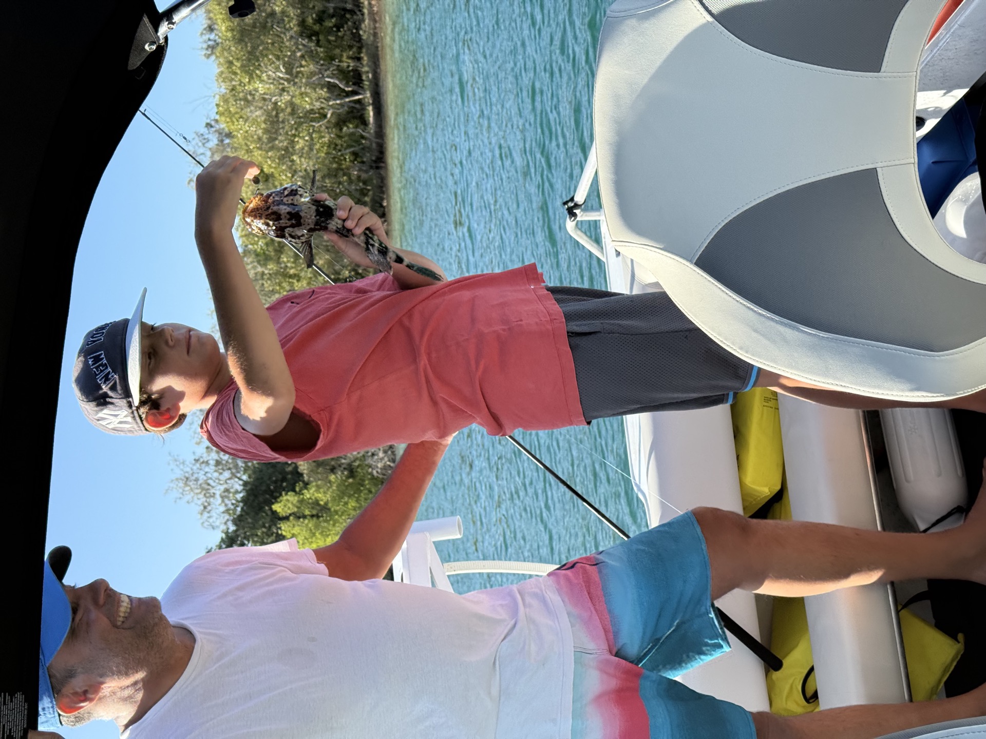 Patrick and his son on a boat, his son holding up a rockcod they just caught