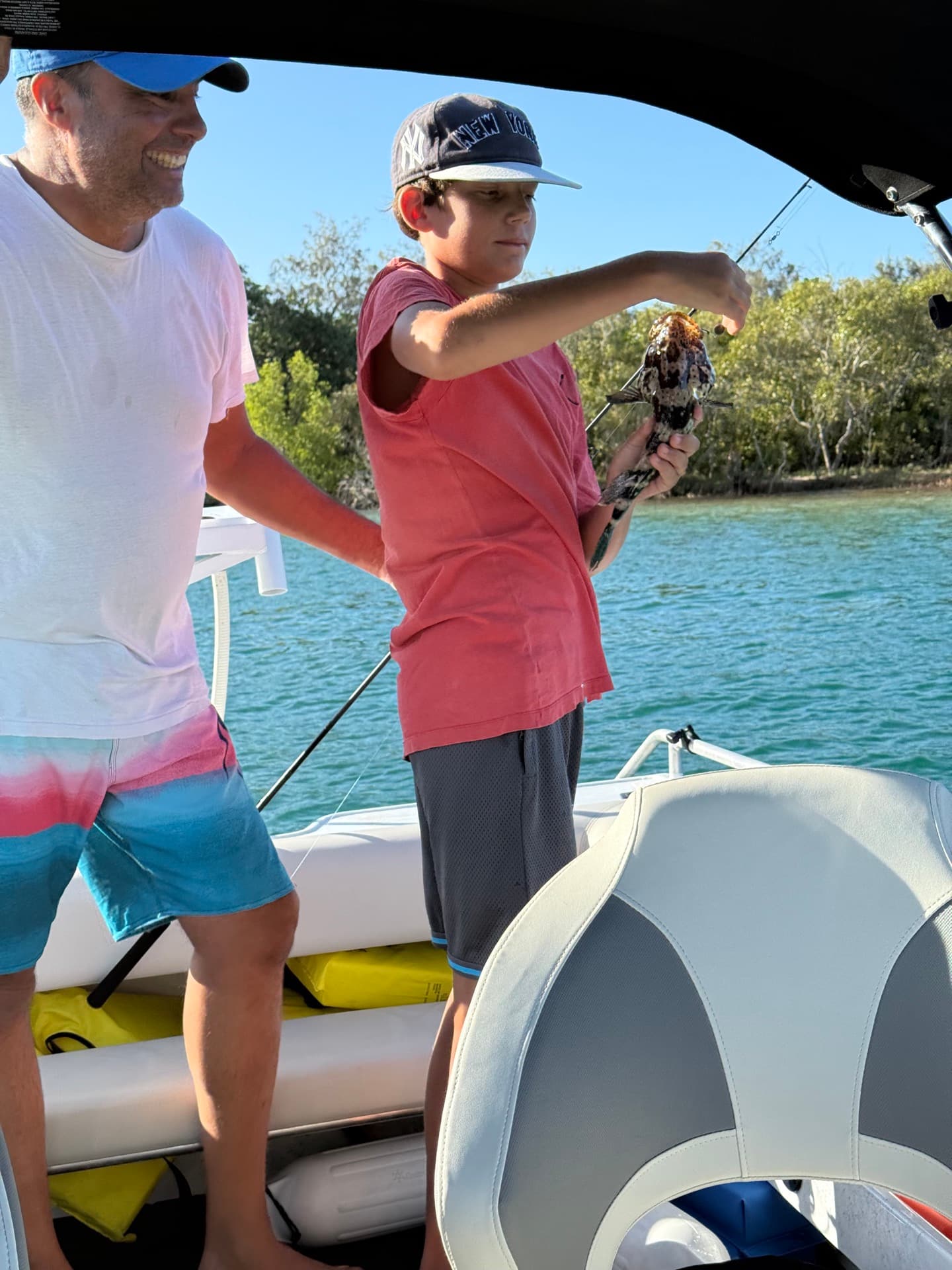 Patrick and his son on a boat, his son holding up a rockcod they just caught