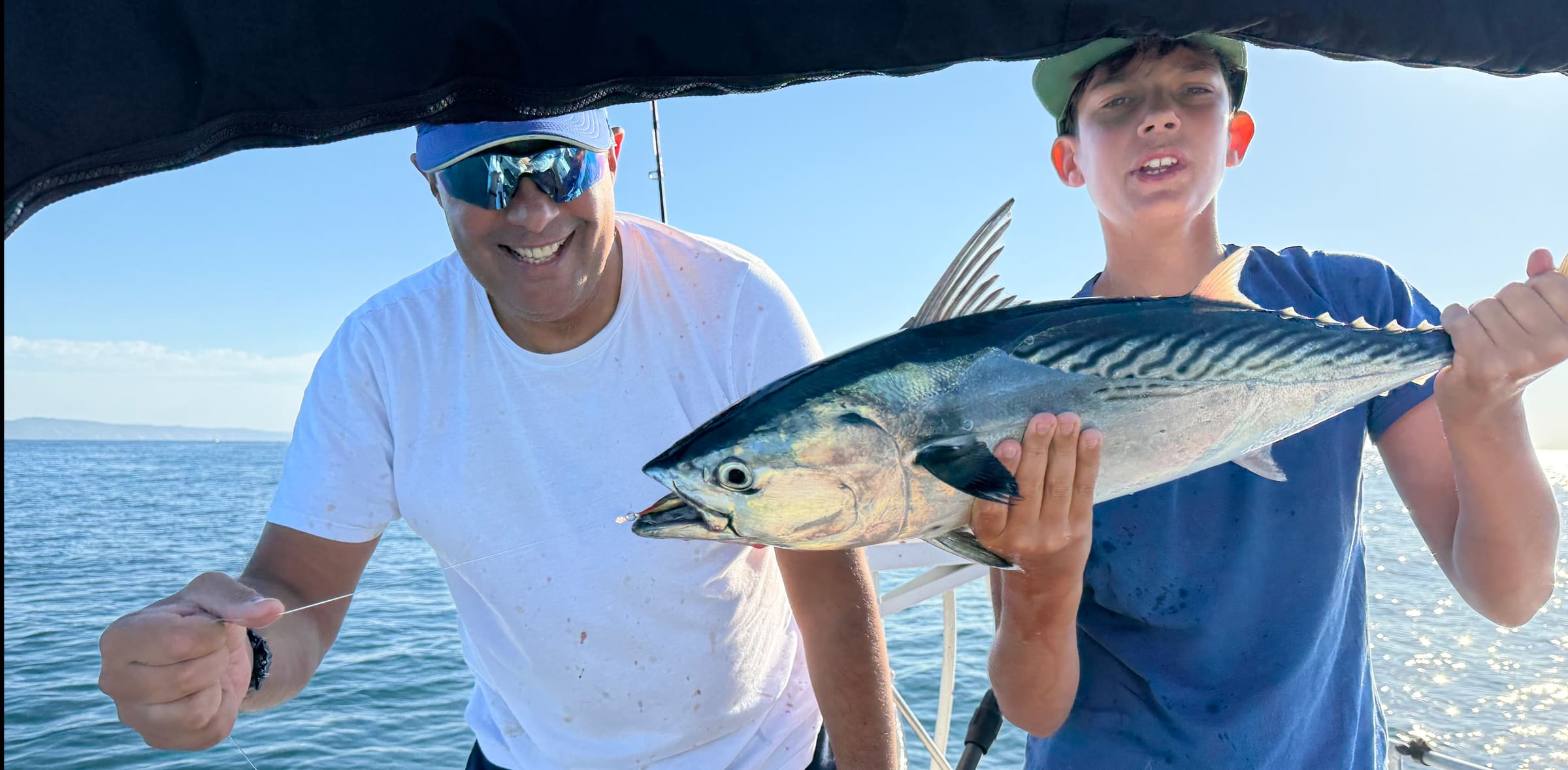 Patrick and his son on a boat, his son holding up a large fish they just caught